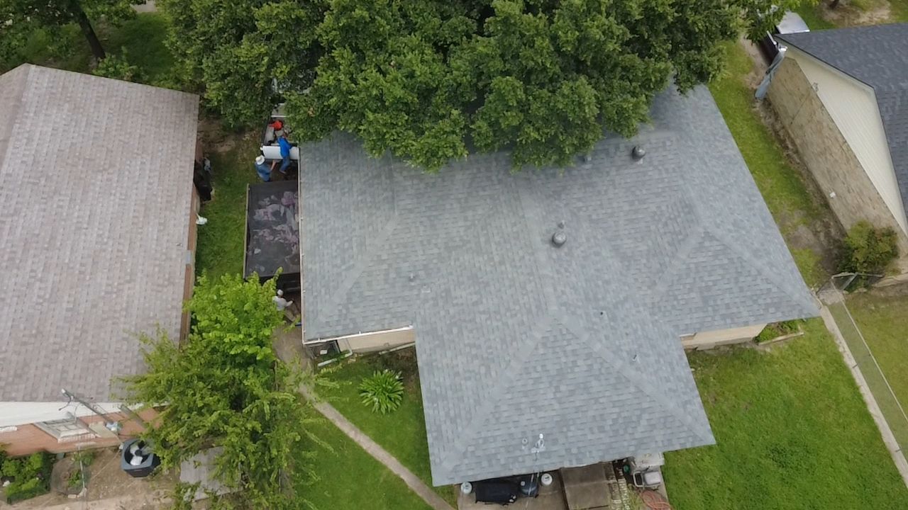 Aerial view of gray shingle roof with debris removal in progress