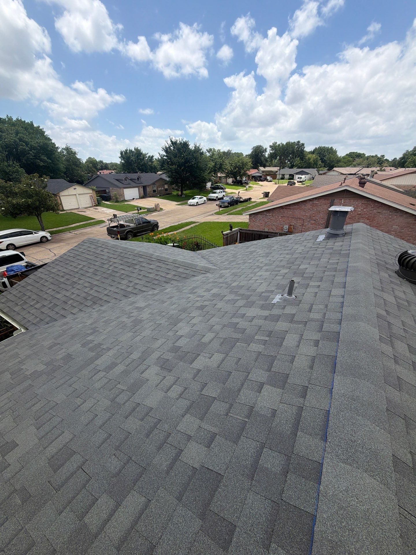 Rooftop view of new gray shingle installation with neighborhood in background